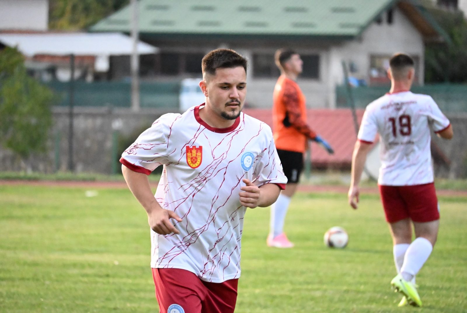 Играч во бело ја носи топката напред, со поглед нагоре
